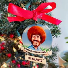 Christmas ornament with a portrait of Bob Ross and a red ribbon, hanging on a decorated Christmas tree.