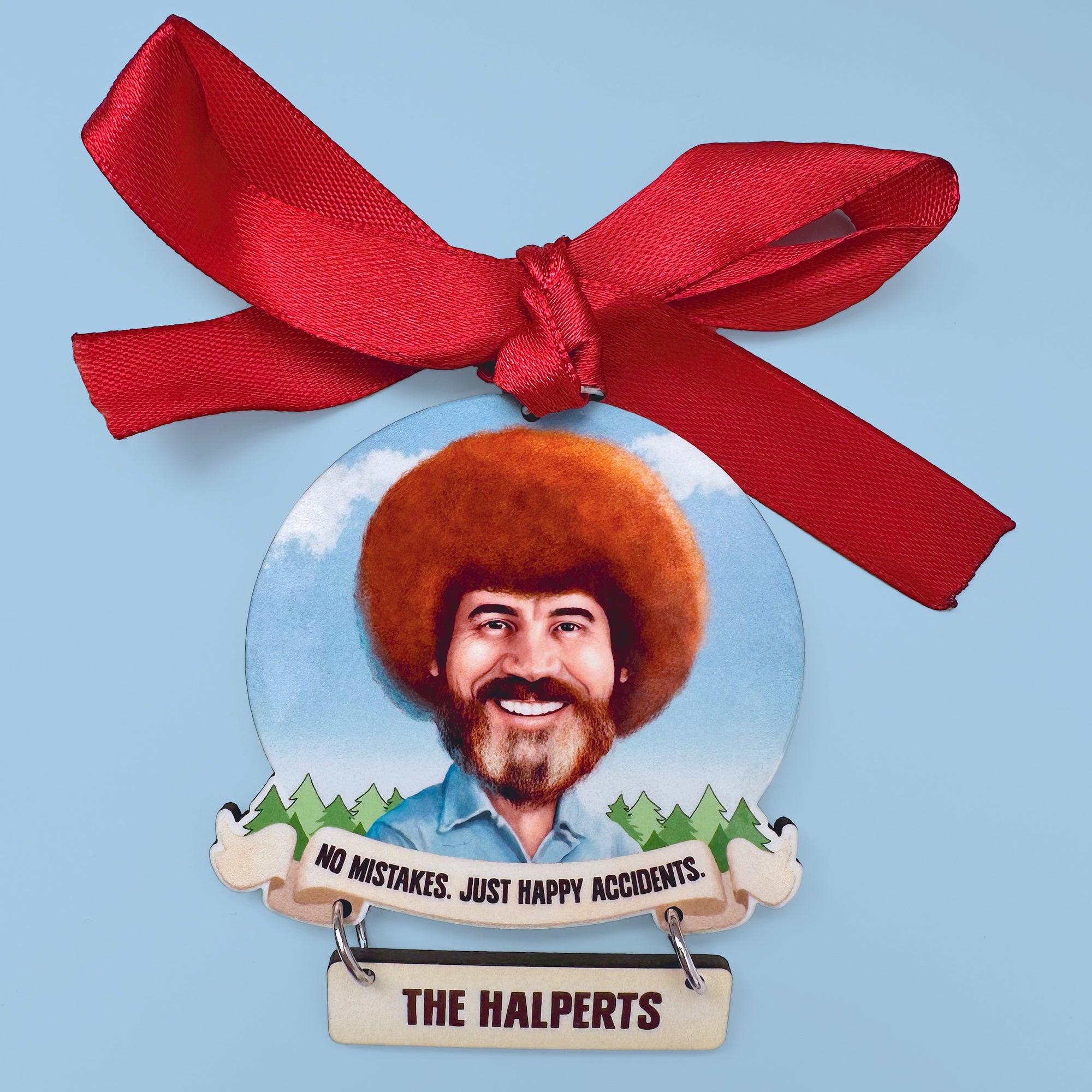 Decorative ornament with a portrait ofBob Ross with a red bow on a light blue background