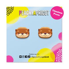 Peachy Apricot otter-shaped earrings on a colorful packaging background