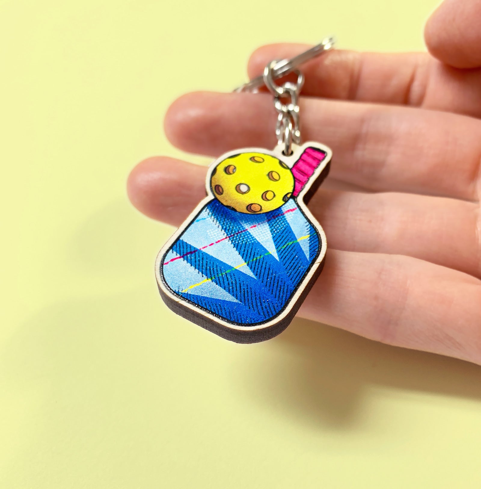 Colorful keychain held in a hand against a yellow background