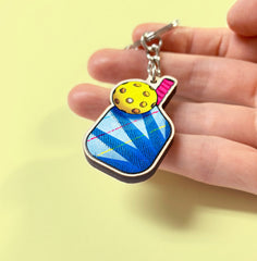 Colorful keychain held in a hand against a yellow background