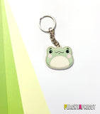  illustration of a cute frog head on a wooden keychain